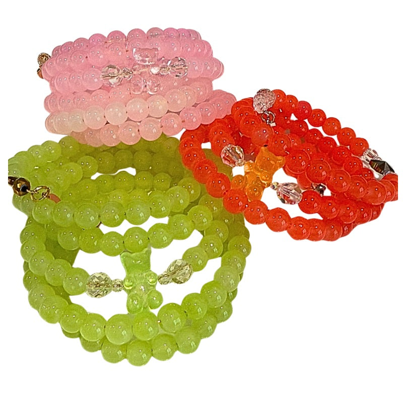Three colorful beaded bracelets in pink, green, and orange on a white background